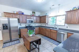 Kitchen with appliances with stainless steel finishes, sink, light tile patterned floors, and decorative light fixtures