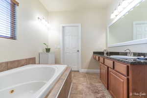 Bathroom with tile patterned flooring, vanity, and tiled bath