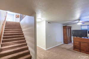 Staircase featuring ceiling fan, carpet, and a textured ceiling