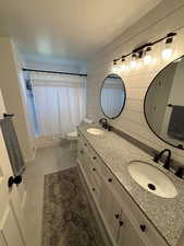 Bathroom featuring tile patterned flooring, wooden walls, vanity, a textured ceiling, and toilet