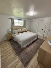 Bedroom with two closets, light hardwood / wood-style floors, and a textured ceiling