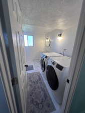 Clothes washing area featuring a textured ceiling and independent washer and dryer