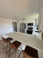 Kitchen with appliances with stainless steel finishes, a breakfast bar area, white cabinets, light hardwood / wood-style floors, and kitchen peninsula