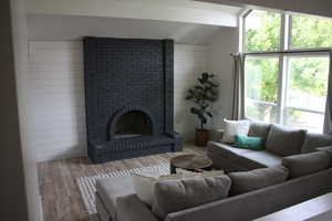 Living room featuring a brick fireplace, wooden walls, lofted ceiling with beams, and light wood-type flooring