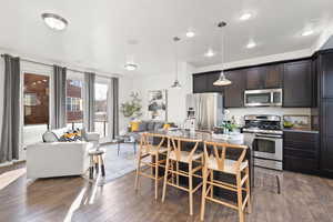 Kitchen with dark hardwood / wood-style floors, pendant lighting, an island with sink, a kitchen bar, and stainless steel appliances