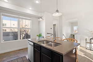 Kitchen featuring dishwasher, sink, hanging light fixtures, light hardwood / wood-style floors, and a center island with sink