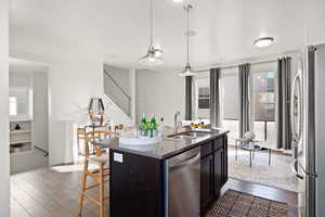 Kitchen with decorative light fixtures, wood-type flooring, sink, a kitchen island with sink, and stainless steel appliances