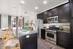 Kitchen with pendant lighting, a kitchen island with sink, dark brown cabinets, stainless steel appliances, and dark hardwood / wood-style floors