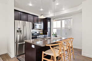 Kitchen with dark brown cabinetry, sink, decorative light fixtures, a center island with sink, and appliances with stainless steel finishes