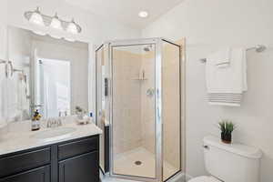 Bathroom featuring vanity, a shower with shower door, lofted ceiling, and toilet