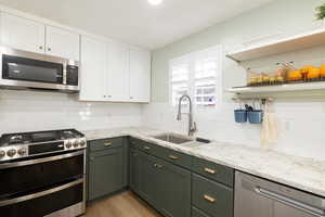 Kitchen with stainless steel appliances,gas range,  light stone countertops, sink, and white cabinets