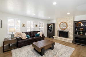 Living room featuring hardwood / wood-style flooring, a brick fireplace, plantation shutters, and a canned lighting.