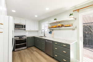 Kitchen with sink, appliances with stainless steel finishes, gas range, white cabinetry, decorative backsplash, and light wood-type flooring