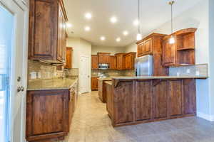 Kitchen featuring light stone counters, decorative backsplash, stainless steel appliances, and kitchen peninsula