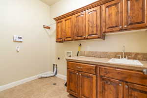 Clothes washing area with sink, cabinets, light tile patterned floors, washer hookup, and hookup for an electric dryer