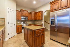 Kitchen featuring decorative backsplash, stainless steel appliances, a center island, and light tile patterned flooring