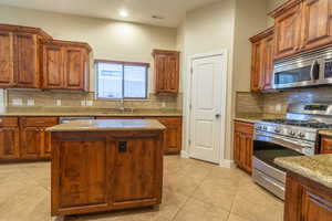 Kitchen with light tile patterned floors, sink, stainless steel appliances, light stone counters, and a kitchen island