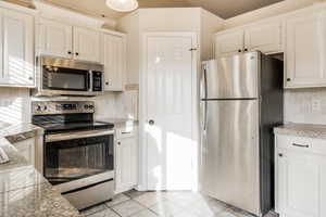 Kitchen featuring white cabinets, light tile patterned flooring, backsplash, and appliances with stainless steel finishes