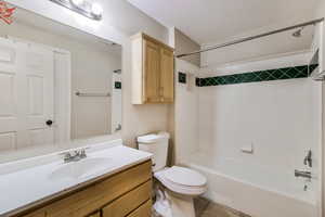 Full bathroom with a textured ceiling, vanity, toilet, and tiled shower / bath combo