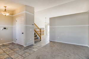 Carpeted empty room with a high ceiling and an inviting chandelier