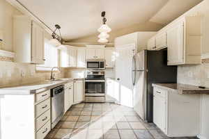 Kitchen featuring sink, stainless steel appliances, backsplash, decorative light fixtures, and lofted ceiling