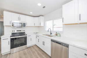 Kitchen featuring sink, stainless steel appliances, light stone countertops, light hardwood / wood-style floors, and white cabinets