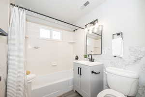 Full bathroom with shower / tub combo with curtain, vanity, toilet, and tile walls