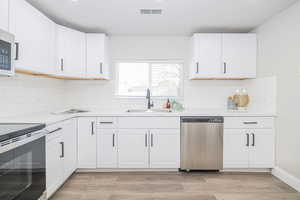 Kitchen with stainless steel appliances, white cabinetry, sink, and light hardwood / wood-style flooring