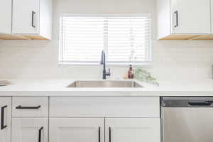 Kitchen with light stone counters, sink, stainless steel dishwasher, and white cabinets