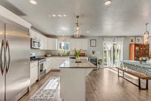 Kitchen with white cabinetry, light stone counters, decorative light fixtures, a center island, and stainless steel appliances