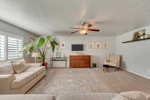 Carpeted living room with a textured ceiling and ceiling fan