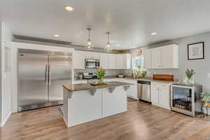 Kitchen featuring stainless steel appliances, white cabinetry, pendant lighting, and beverage cooler