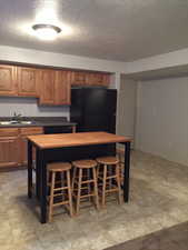 Kitchen with a breakfast bar, sink, black fridge, wooden counters, and a textured ceiling