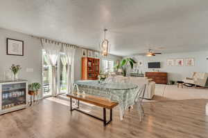 Dining area featuring ceiling fan with notable chandelier, wood-type flooring, and a textured ceiling