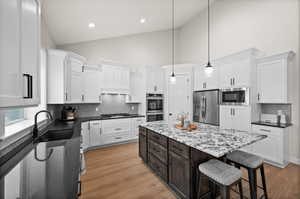 Kitchen with white cabinetry, a center island, high vaulted ceiling, hanging light fixtures, and appliances with stainless steel finishes