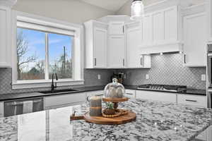 Kitchen with white cabinetry, appliances with stainless steel finishes, sink, and decorative light fixtures