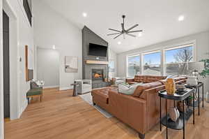 Living room with ceiling fan, a tiled fireplace, high vaulted ceiling, and light hardwood / wood-style flooring