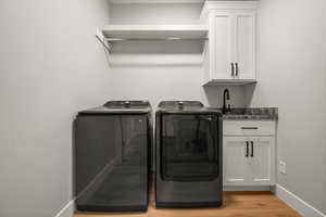 Laundry room with sink, light hardwood / wood-style floors, cabinets, and washing machine and clothes dryer