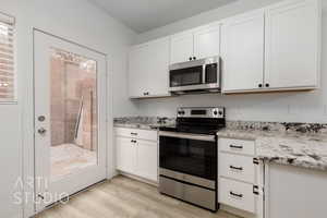 Kitchen with white cabinetry, stainless steel appliances, light stone countertops, and light hardwood / wood-style floors