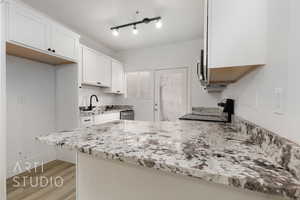 Kitchen featuring white cabinetry, sink, stainless steel appliances, light stone countertops, and light hardwood / wood-style flooring