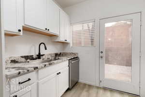 Kitchen with white cabinetry, sink, stainless steel dishwasher, and light stone counters