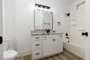 Full bathroom with hardwood / wood-style flooring, vanity, toilet, and shower / bath combination