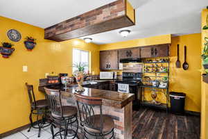 Kitchen with sink, a breakfast bar, dark brown cabinets, black range with electric cooktop, and kitchen peninsula