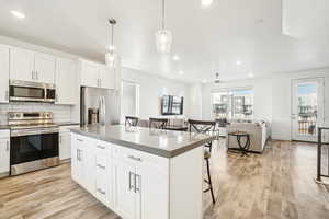 Kitchen with appliances with stainless steel finishes, decorative light fixtures, a breakfast bar area, white cabinets, and a center island