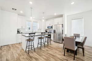 Kitchen with appliances with stainless steel finishes, backsplash, light hardwood / wood-style floors, white cabinets, and decorative light fixtures