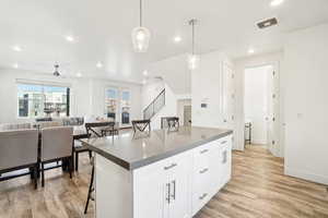 Kitchen featuring a breakfast bar, white cabinets, hanging light fixtures, a center island, and light hardwood / wood-style floors