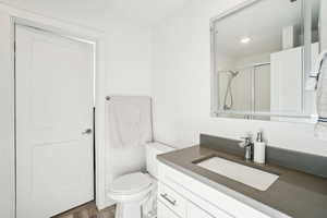 Bathroom with vanity, hardwood / wood-style floors, a shower with shower door, and toilet