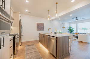 Kitchen with appliances with stainless steel finishes, an island with sink, sink, hanging light fixtures, and light hardwood / wood-style floors