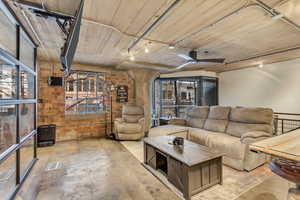 Living room featuring rail lighting, brick wall, retractable mounted TV, and ceiling fan