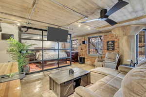 Living room with ceiling fan, track lighting, retractable mounted TV and brick wall